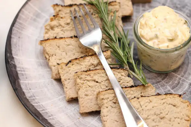 Pokrojony pasztet na talerzu z widelcem, gałązką rozmarynu i słoiczkiem sosu.