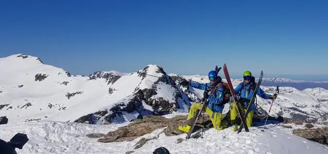 Dwóch narciarzy w kaskach i goglach na szczycie ośnieżonej góry, gotowych do zjazdu. To ich skipass do wolności!