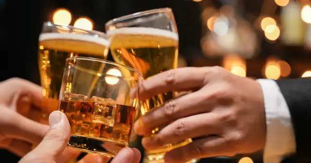 Trzy dłonie wznoszą toast: jedna z whisky na lodzie, dwie z piwem. Lepiej 2 drinki czy 2 piwa?