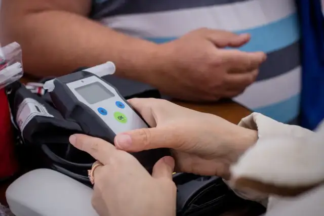 Dłonie trzymające alkomat z widocznym ustnikiem i przyciskami.