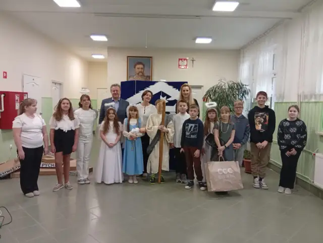 Dzieci w strojach aniołów i pasterzy, odgrywające baśń o dobrym synku. W tle portret i dekoracje.