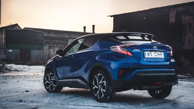 Niebieska Toyota C-HR Hybrid na tle opuszczonych budynków. Czy wybrać hybrydę czy benzynę?