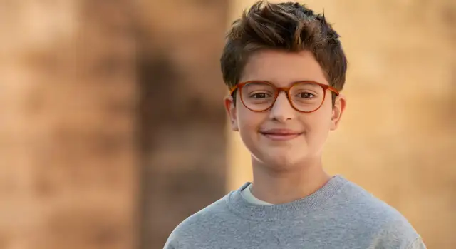 Uśmiechnięty chłopiec w okularach korekcyjnych na tle ceglanej ściany.