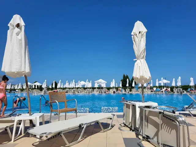 Basen hotelowy z leżakami i parasolami pod błękitnym niebem.