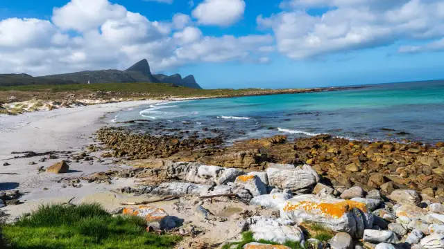 Plaża i skaliste wybrzeże na Przylądku Dobrej Nadziei. Turkusowa woda, piaszczysta plaża, góry w tle.