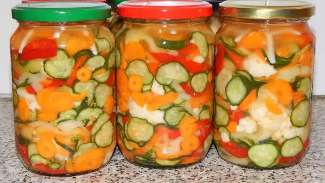 Trzy słoiki z marynowanymi warzywami: ogórkami, marchewką, papryką i kalafiorem.