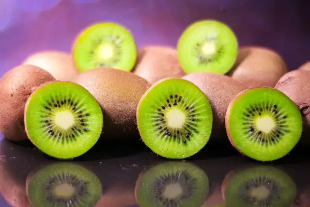 Kilka przekrojonych i całych kiwi na ciemnym tle z fioletowym rozmyciem w tle.