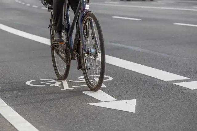 Rowerzysta na ścieżce rowerowej z białymi oznaczeniami kierunku jazdy.