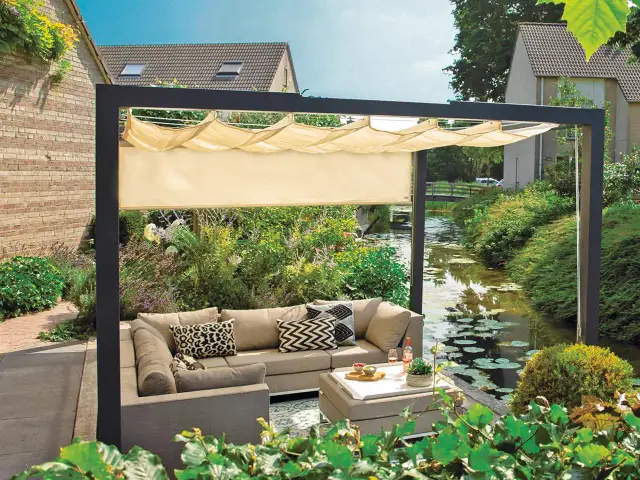 Nowoczesna pergola z wysuwanym daszkiem to idealny sposób, jak osłonić taras od wiatru i słońca. Wygodny narożnik i stolik zachęcają do relaksu.