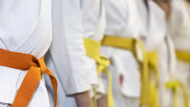 Zbliżenie na białe kimona z pomarańczowym i żółtym pasem, symbolizujące sztuki walki.