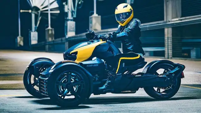 Kierowca w żółtym kasku na futurystycznym motorze trójkołowym Can-Am, gotowy do jazdy.