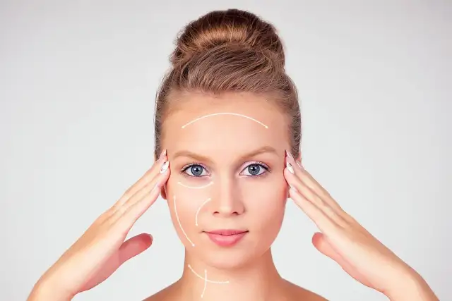 Młoda kobieta z włosami upiętymi w kok, z białymi strzałkami wskazującymi kierunek masażu twarzy.
