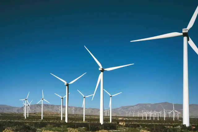 Wiatraki energetyczne na tle błękitnego nieba i gór. W oddali widać kolejne turbiny.