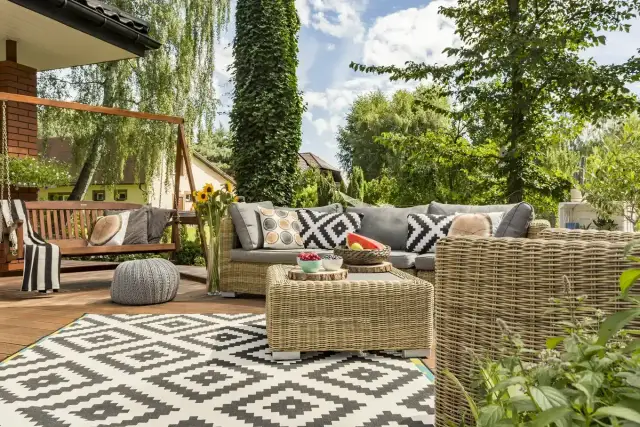 Relaks na tarasie w stylu boho: wiklinowe meble, huśtawka, wzorzysty dywan i mnóstwo zieleni.