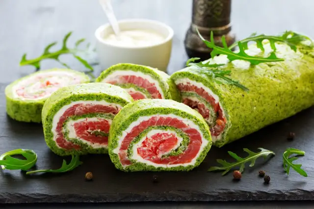 Rolada szpinakowa z mrożonego szpinaku z łososiem i serkiem, pokrojona w plastry, ozdobiona rukolą.