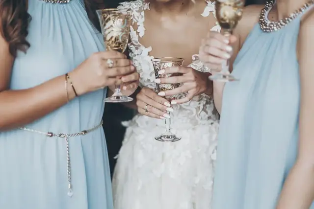 Panna młoda i druhny w błękitnych sukniach wznoszą kieliszki do toastu.