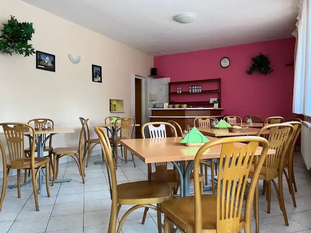 Wnętrze restauracji z drewnianymi stołami i krzesłami, różową ścianą i zielonymi roślinami.