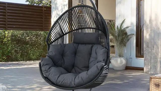 Czarny, wiszący fotel w kształcie kokonu, z miękkimi, szarymi poduszkami, idealny do relaksu na tarasie.