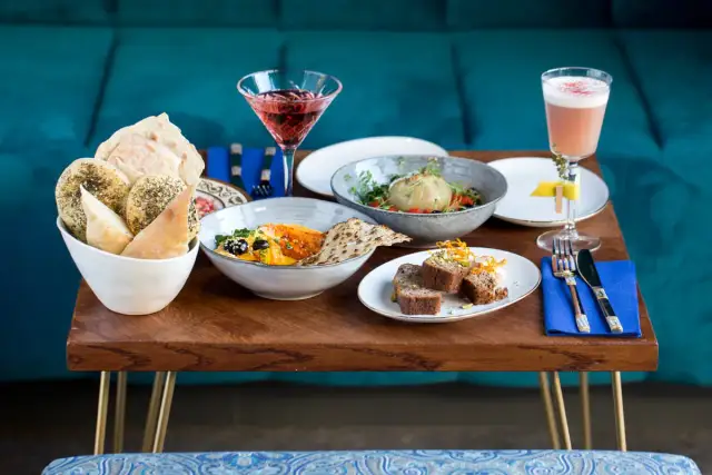 Stół z jedzeniem: pieczywo, hummus, sałatka, ciasto i drinki.