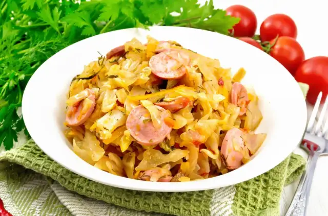 Pyszny bigos z młodej kapusty z kiełbasą, podany na białym talerzu, ozdobiony zieloną natką i pomidorkami.