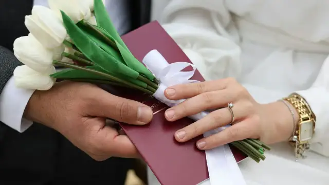 Dłoń mężczyzny i kobiety trzymają bukiet białych tulipanów i czerwony dokument.