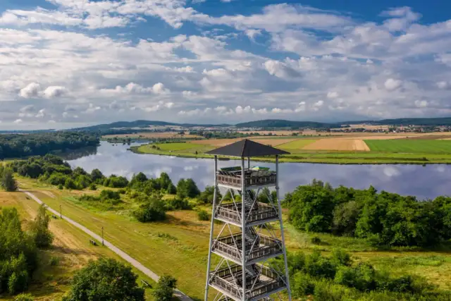 Wieża widokowa nad jeziorem, otoczona zielenią i polami uprawnymi.