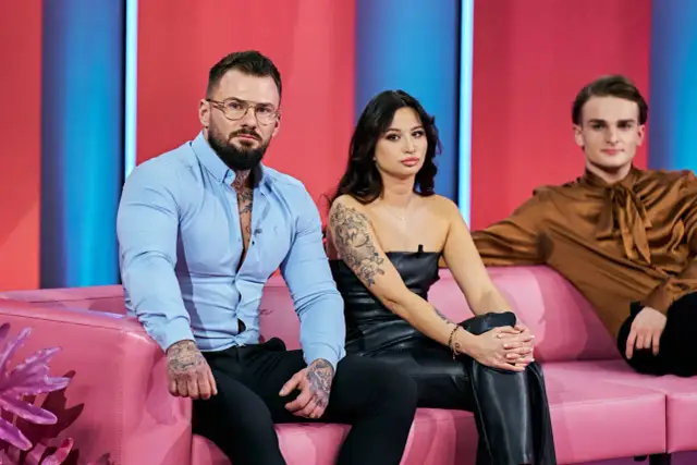 Uczestnicy "Love Never Lies Polska" siedzą na różowej kanapie. Mężczyzna w niebieskiej koszuli i kobieta w czarnym topie mają tatuaże.