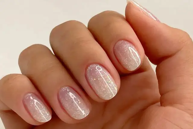 Nahaufnahme einer Hand mit ovalen Nägeln, die mit schimmerndem Glitzer-Nagellack in Pastelltönen verziert sind.