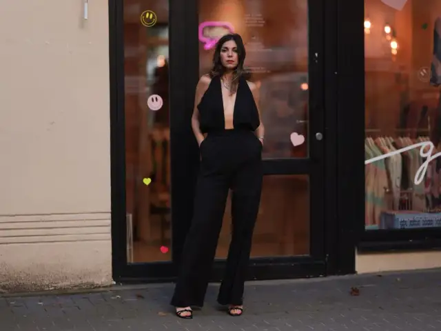 Elegancka kobieta w czarnym, głęboko wyciętym kombinezonie. Idealna inspiracja, co założyć do czarnego kombinezonu na wieczór.