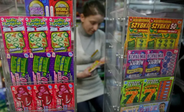 Zdrapki "Pieniądze jak lodu" i inne losy na loterii w kiosku. Kobieta wybiera zdrapkę.