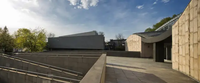 Nowoczesna architektura muzeum sztuki i techniki japońskiej Manggha z kamiennymi fasadami i zielenią w tle.