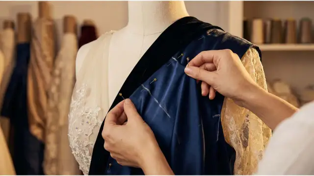 Krawcowa dopina granatowy materiał, przypominający szyfon, do sukni ślubnej.