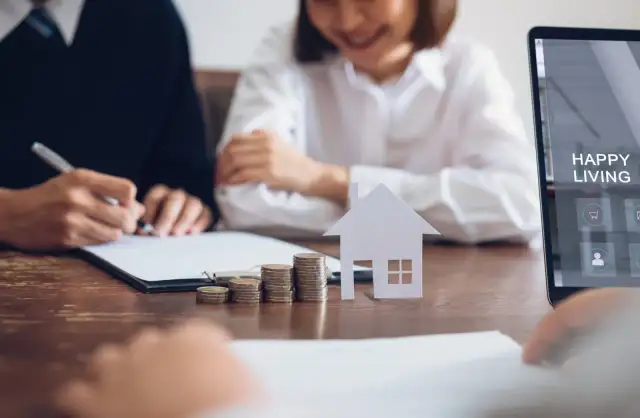 Para z podpisem dokumentów, monety, model domu i tablet z napisem "Happy Living".