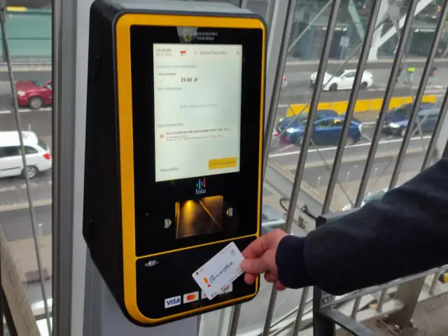 Ręka zbliża kartę "Pomorskie" do biletomatu.