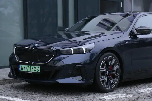 Eleganckie bmw serii 5 w ciemnym kolorze, z charakterystycznym grillem i sportowymi felgami, zaparkowane na brukowanej nawierzchni.