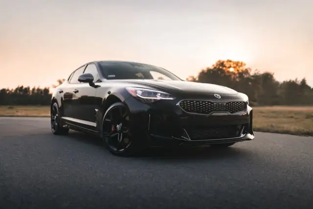 Czarna Kia Stinger, sportowy samochód z Korei Południowej, zaparkowana na pustej drodze o zachodzie słońca.
