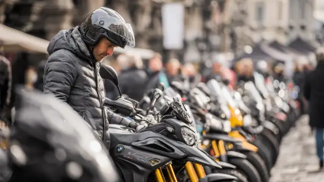 Mężczyzna w kasku ogląda lekki motocykl. W tle rząd innych motocykli i ludzi.