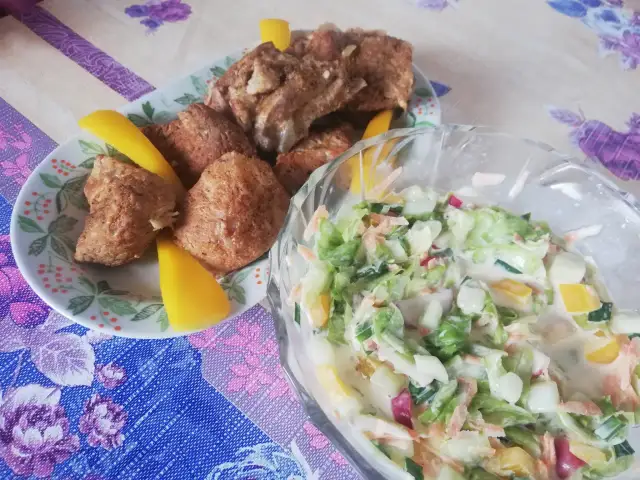 Talerz z żeberkami i kawałkami żółtej papryki obok miski z kolorową surówką.