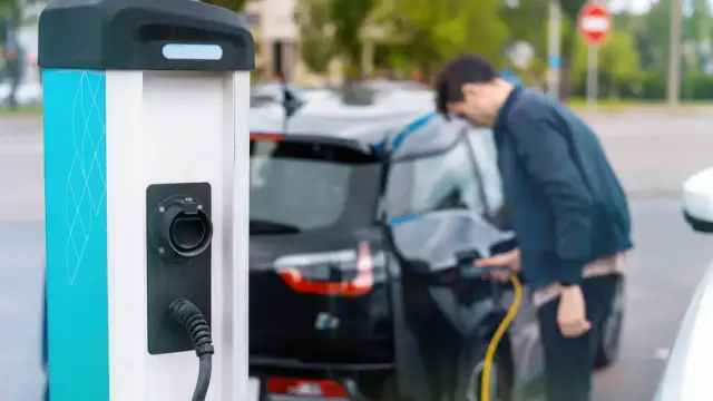 Mężczyzna ładuje czarny samochód elektryczny przy stacji ładowania.
