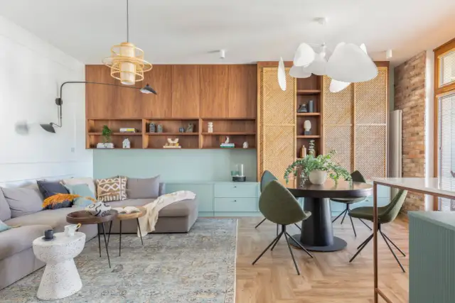 Przytulny, mały pokój w stylu boho z szarą kanapą, drewnianymi meblami i plecionymi elementami.