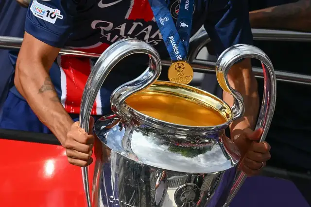 Piłkarz trzyma Puchar Ligi Mistrzów, marząc o tym, kto wygra ligę mistrzów. Złoty medal wisi na jego szyi.