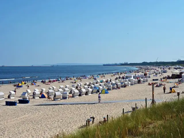 Plaża nad Bałtykiem z rzędami koszy plażowych, ludźmi i morzem w tle.