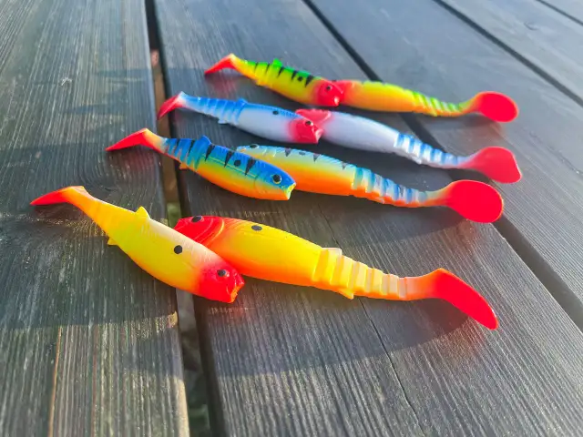 Kolorowe przynęty na spinning, imitujące rybki, leżą na drewnianym stole.