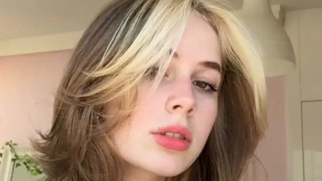 Dziewczyna z modnym wolf cut bez grzywki, z pasemkami blond na ciemniejszych włosach.