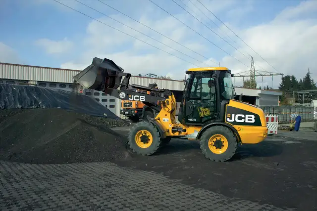 Żółta ładowarka JCB 406 z podniesioną łyżką, gotowa do pracy. Dane techniczne tej maszyny pozwalają na efektywne przenoszenie materiałów.