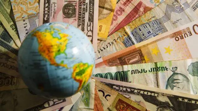 Mała kula ziemska na tle różnych walut świata.