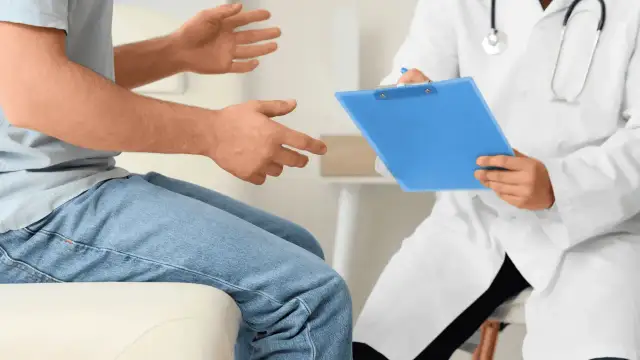 Pacjent rozmawia z lekarzem, który notuje coś na niebieskiej teczce.