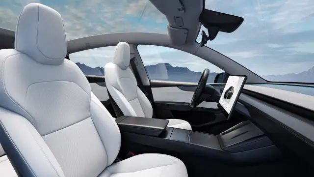 Wnętrze samochodu Tesla z białymi skórzanymi fotelami i dużym ekranem dotykowym.
