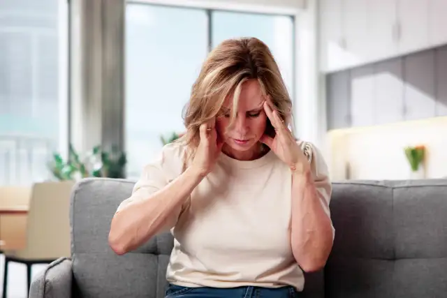 Kobieta z bólem głowy, trzymająca się za skronie, siedząca na kanapie.