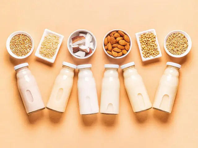 Butelki z mlekiem roślinnym i miseczki z migdałami, ryżem, kokosem, soją i owsem.